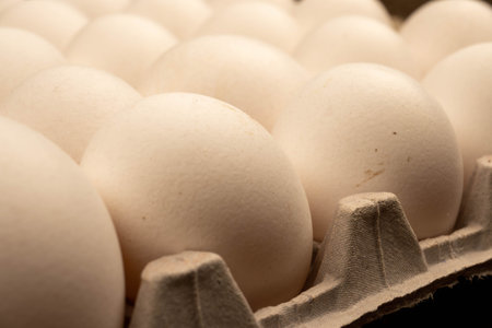 White chicken eggs in a cardboard box on the table. Close-up, selective focus.