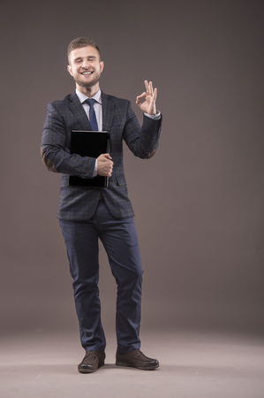 Businessman standing in suit with laptop in his hands and showing sign of okの写真素材