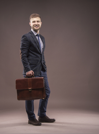 Young man smiling in a suit with a briefcase in his handsの写真素材