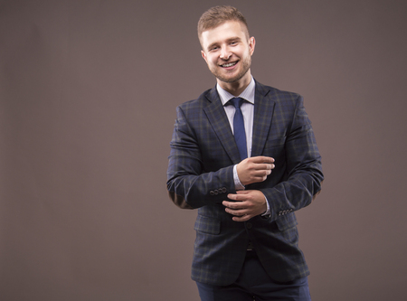 Young man in suit adjusts his cuffs and smilingの写真素材