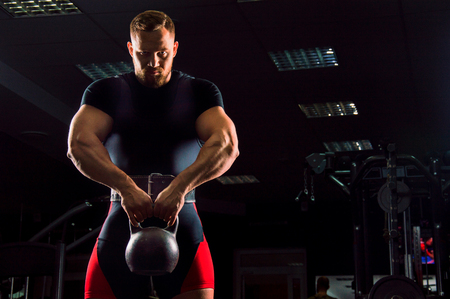 Huge weightlifter stands with a weight in his hands in the gymの写真素材