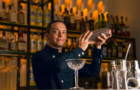 Barman with a charming smile prepares a delicious drink by shakingの写真素材