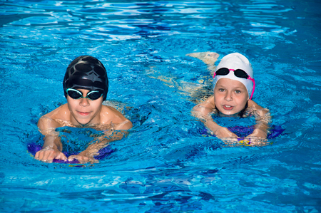 Little children swim in the pool under the guidance of a coachの写真素材
