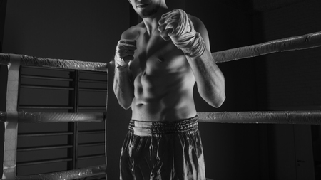 Kickboxer stands in the corner of the ring in an attacking rack with bandages on his handsの写真素材