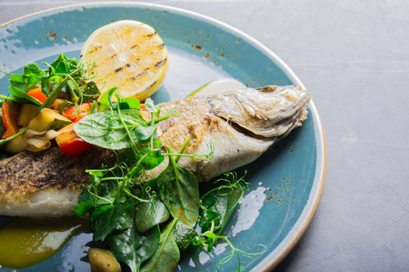 Grilled whole seabass with vegetable garnish. View from aboveの写真素材