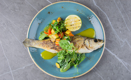 Grilled whole seabass with vegetable garnish. View from aboveの写真素材