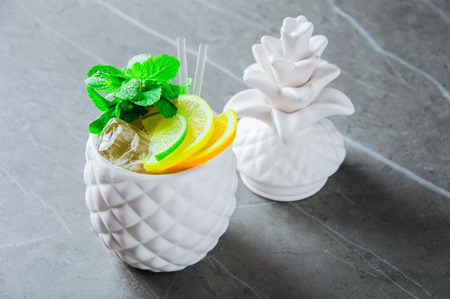 Delicious exotic cocktail in a glass in the form of pineapple. Decorated with mint leaves and slices of lime and orangeの写真素材