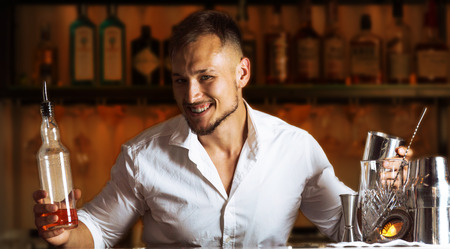 Fantastically beautiful guy smiles into the camera and holds a bottle and a shaker in his hands. Mixed mediaの写真素材
