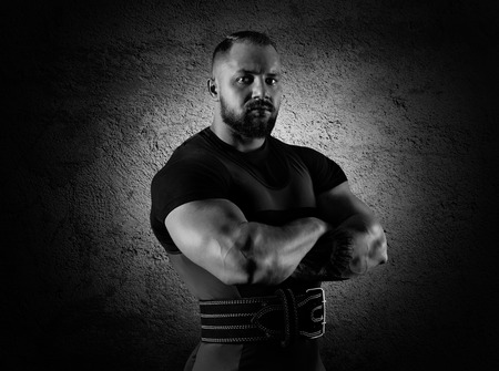 The weightlifter stands in a menacing pose with crossed huge arms and looks at the cameraの写真素材