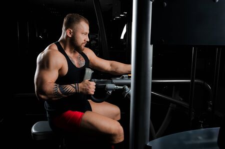 The athlete performs an exercise on the latissimus muscles of the back on a special device. Side viewの写真素材