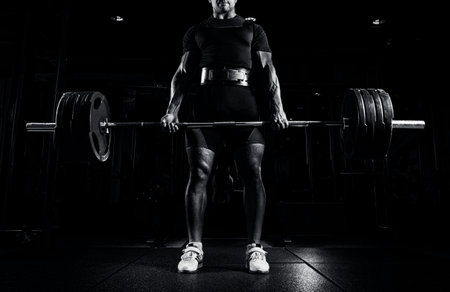 Professional athlete is standing and is holding a very heavy barbell. Front view