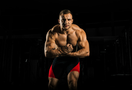 The weightlifter is posing in front of the camera, monstrously straining his arms as he screams from the tension. Front viewの写真素材