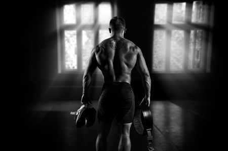 The athlete goes to the gym for training. In his hands he holds sneakers and a belt. Back viewの写真素材