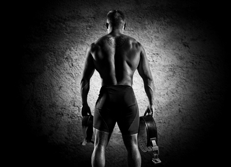 The athlete goes to the gym for training. In his hands he holds sneakers and a belt. Back viewの写真素材