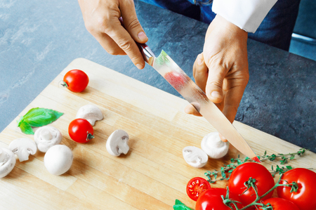 Professional chef cuts vegetables with a sharp knife from Damascus steel. Mixed mediaの写真素材