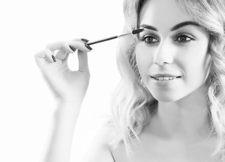 Charming young girl paints eyebrows with a long professional brush. Mixed media