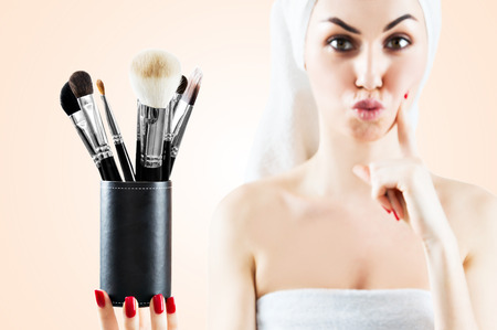 Young charming girl with a white towel on her head is holding a set of brushes for make-up and is trying to make a choice. Mixed mediaの写真素材