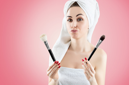 Young charming girl with a white towel on her head holds two brushes for make-up and tries to make a choice. Mixed mediaの写真素材