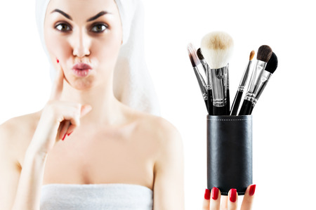 Young charming girl with a white towel on her head is holding a set of brushes for make-up and is trying to make a choice. Mixed mediaの写真素材