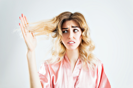 The charming girl looks with horror at the split ends of her hair. Mixed mediaの写真素材