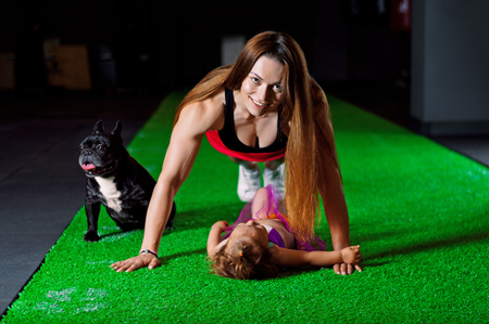 Charming sports mom plays in the gym with her little daughter and a French bulldog. Mixed mediaの写真素材