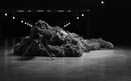 The sniper in disguise lies with a sniper rifle and aims at the telescopic sight.の写真素材