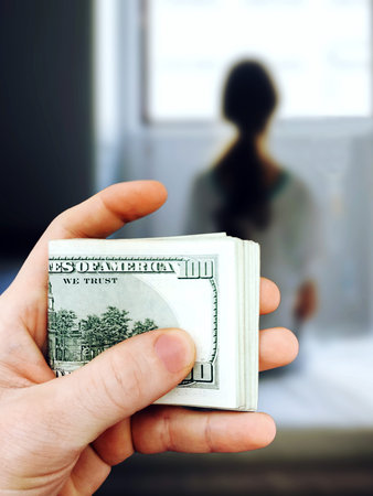 Man holds in his hand a bundle of one hundred dollar bills against the background of the girl who...