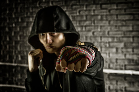 Boxer in a black sweatshirt and bandages wound on his hands beats his fist forward. The concept of...