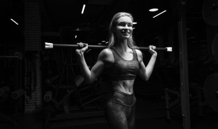 Charming blonde posing in the gym with a body-bar. Front view. The concept of sports, bodybuilding, fitness. Mixed mediaの写真素材