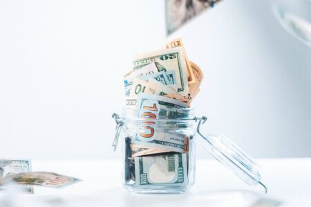 Glass piggy bank full of money. Banknotes are strewed from above. The concept of squandering. Mixed mediaの写真素材
