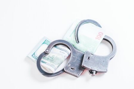 Packs of euros and hundred dollar bills are enclosed in handcuff bracelets. The concept of theft, fraud and illegal business. Corruption. Mixed mediaの写真素材