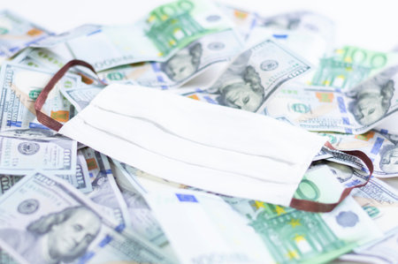 Medical mask rests on one hundred dollar bills. The concept of an epidemic, paid medicine, lack of...