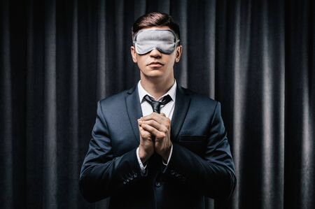 Portrait of a man in a mask for sleeping. He prays against a black curtain. The concept of blind dates, dating on social networks. Mixed mediaの写真素材