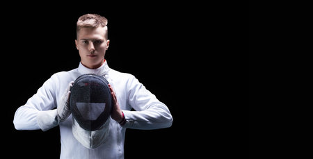 Portrait of a male fencer on a black background. He holds a helmet in front of him. The concept of...