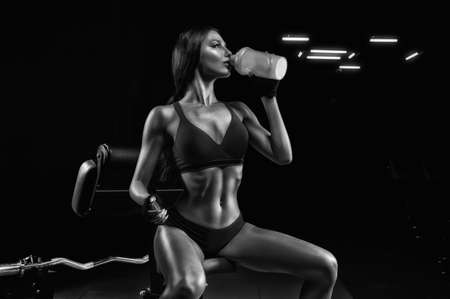 Beautiful tall athlete sits on a bench and drinks from a shaker. Bodybuilding and sports nutrition concept. Mixed mediaの写真素材