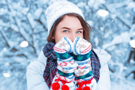 Portrait of a beautiful woman against the background of a winter forest in New Year's mittens....