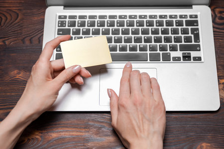 Image of female hands with a gold bank card. The girl enters the card number on the website....