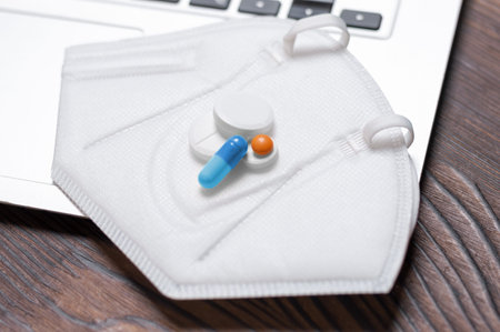 Image of a laptop and a protective medical mask with pills. Concept of online consultation with a...
