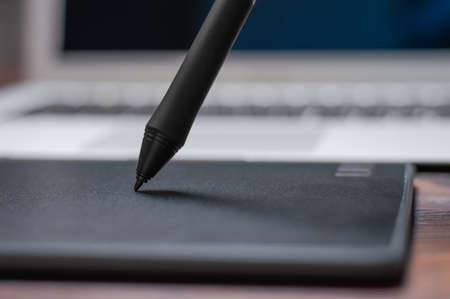 Image of a graphics tablet, stylus and laptop on a wooden table. Designer workplace. Freelance. Retouching. IT concept. Mixed mediaの写真素材