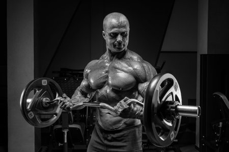 Professional weightlifter posing in the gym with a barbell in his hands. Classic bodybuilding. Mixed mediaの写真素材