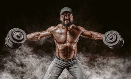 Muscular athlete lifts dumbbells. Shoulder pumping. Fitness and bodybuilding concept. Mixed mediaの写真素材