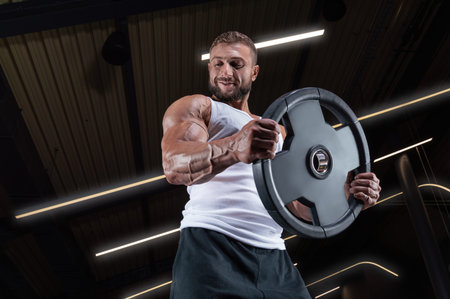 Portrait of a man in a white T-shirt exercising in the gym with barbell discs. Biceps pumping....