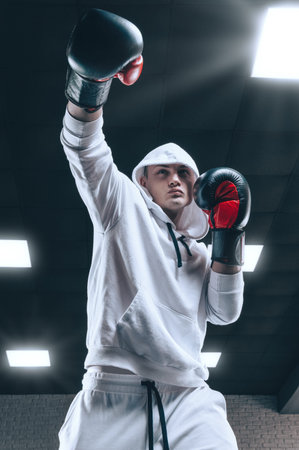 Brutal athlete boxing in the ring in a white hoodie covered with a hood. Mixed martial arts concept....