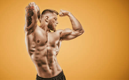 Young muscular guy with nice abs posing on an orange background. Fitness and nutrition concept. Mixed mediaの写真素材