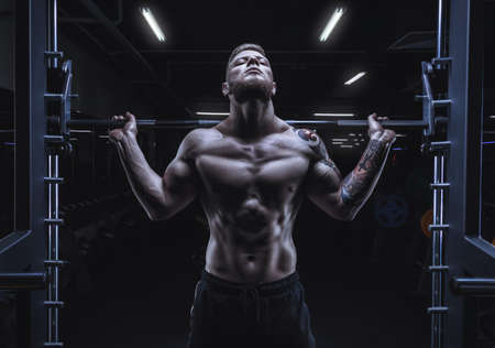 Portrait of an athlete with a barbell on the shoulders of the gym. Bodybuilding and fitness concept. Mixed mediaの写真素材