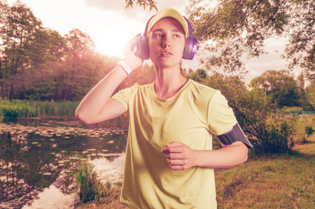 Portrait of a beautiful girl running in a sunny park in headphones with a smartphone. Music apps...