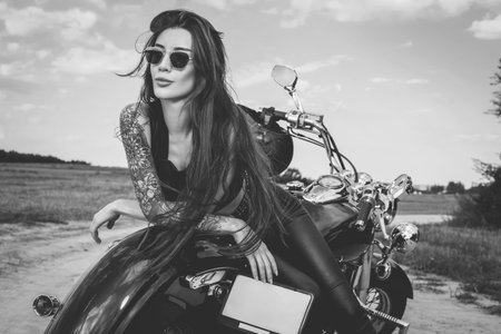 Sexy girl in a leather suit posing near a motorcycle at sunset. Travel concept. Mixed mediaの写真素材
