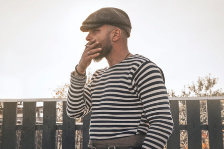 Handsome bearded man in a cap smokes before hunting. Duck hunting season concept. Mixed media