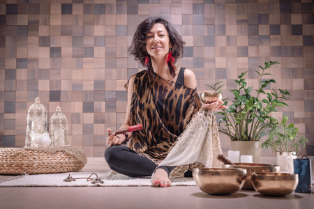 Image of an adult woman in yoga place. Playing on Tibetan singing bowls. The concept of yoga and spiritual practices. Mixed mediaの写真素材