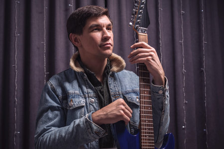 Man in a denim jacket plays a blue electric guitar. Concerts concept. Mixed media